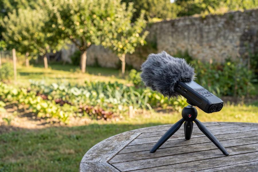 Un enregistreur muni d’une bonnette, posé sur une table de jardin face à un potager