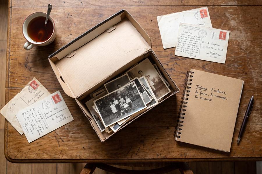 Une boîte à chaussures remplie de vieilles photos, des cartes postales et un carnet où sont notés les thèmes de l’entretien, sur la table de la salle à manger